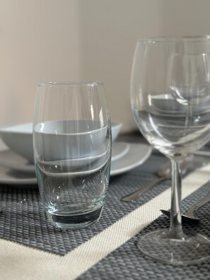 A table setting with two clear wine glasses and a white bowl on a woven placemat.