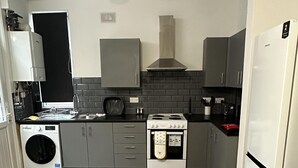 A compact kitchen with grey cabinets, a stove, a washing machine, and a refrigerator. - Cosy Manchester House Near Etihad and Coop Live (Manchester)
