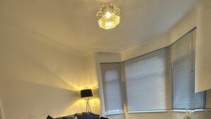 A modern living room with a sofa, a coffee table, a lamp, and a large window with blinds. - Cosy Manchester House Near Etihad and Coop Live (Manchester)