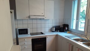 Een compacte keuken met witte kastjes, een magnetron, een koffiezetapparaat en een vaatwasser.