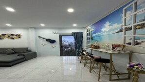 A modern living room with a grey sofa, a dining area with wooden chairs, a guitar wall art, and a beach mural. - Homestay BNB (Ho Chi Minh City)