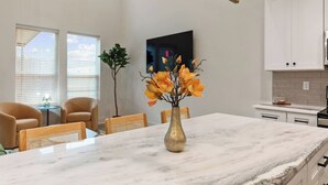A modern kitchen with white cabinets, a marble countertop, and a vase with flowers.