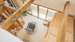 A spacious living area with a wooden staircase, a black chair, and a potted plant. - ReVIERA Resort Villa (Chatan)