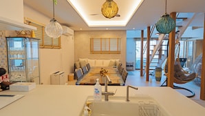 A modern kitchen with a central island, a dining area with a glass table, and a hanging chair. - ReVIERA Resort Villa (Chatan)