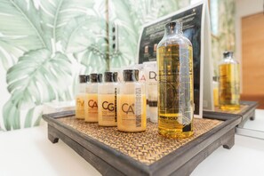A display of body soap bottles on a wooden tray with a tropical plant background. - ReVIERA Resort Villa (Chatan)