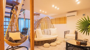 A modern living room with a hanging chair, a round sofa, a coffee table, and a large plant. - ReVIERA Resort Villa (Chatan)