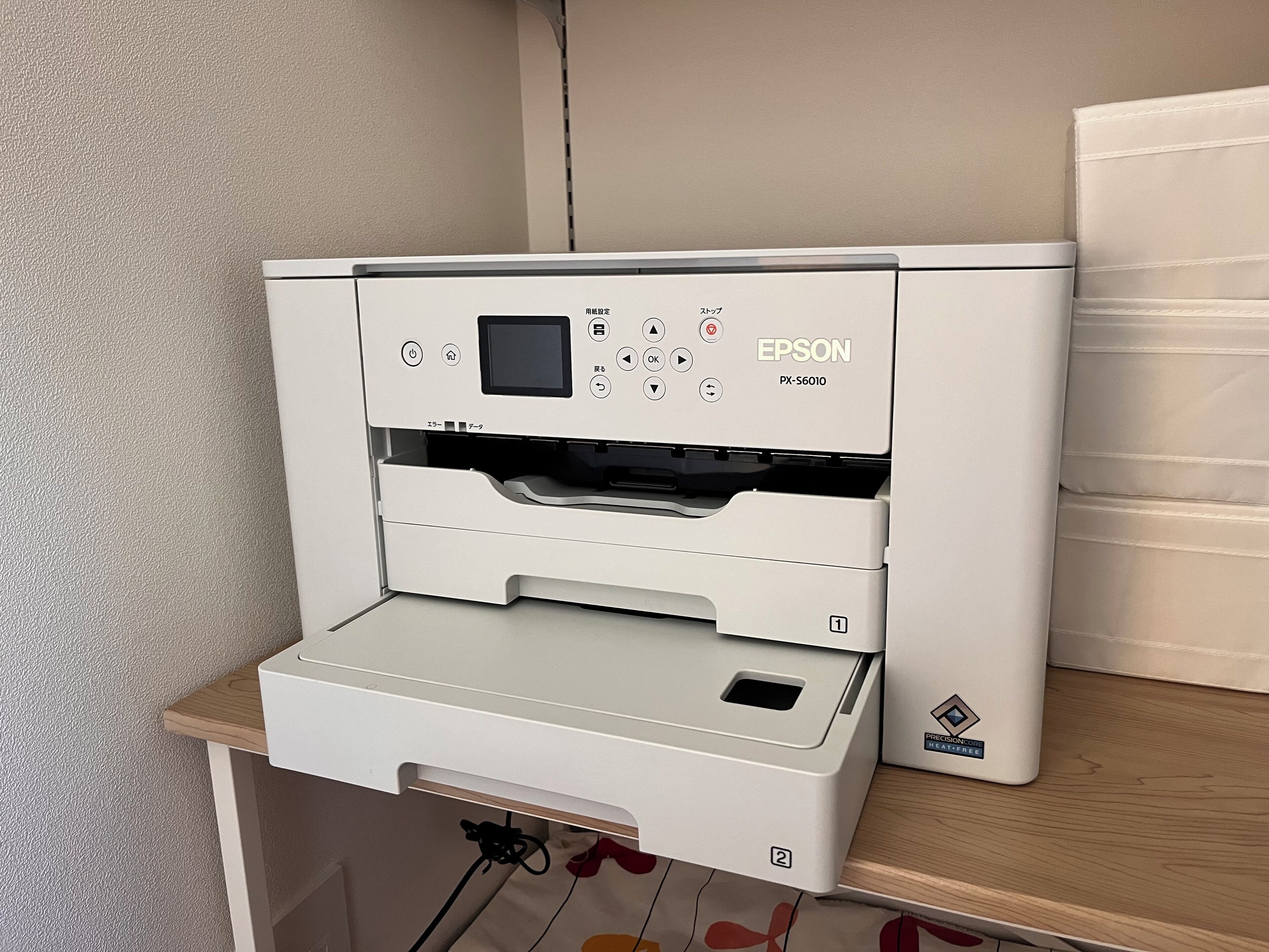 A white Epson printer on a wooden table with a beige wall in the background.