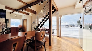 Un comedor amplio con una mesa y sillas de madera, una escalera que sube a un nivel superior, y un gran ventanal con vistas a un paisaje nevado.