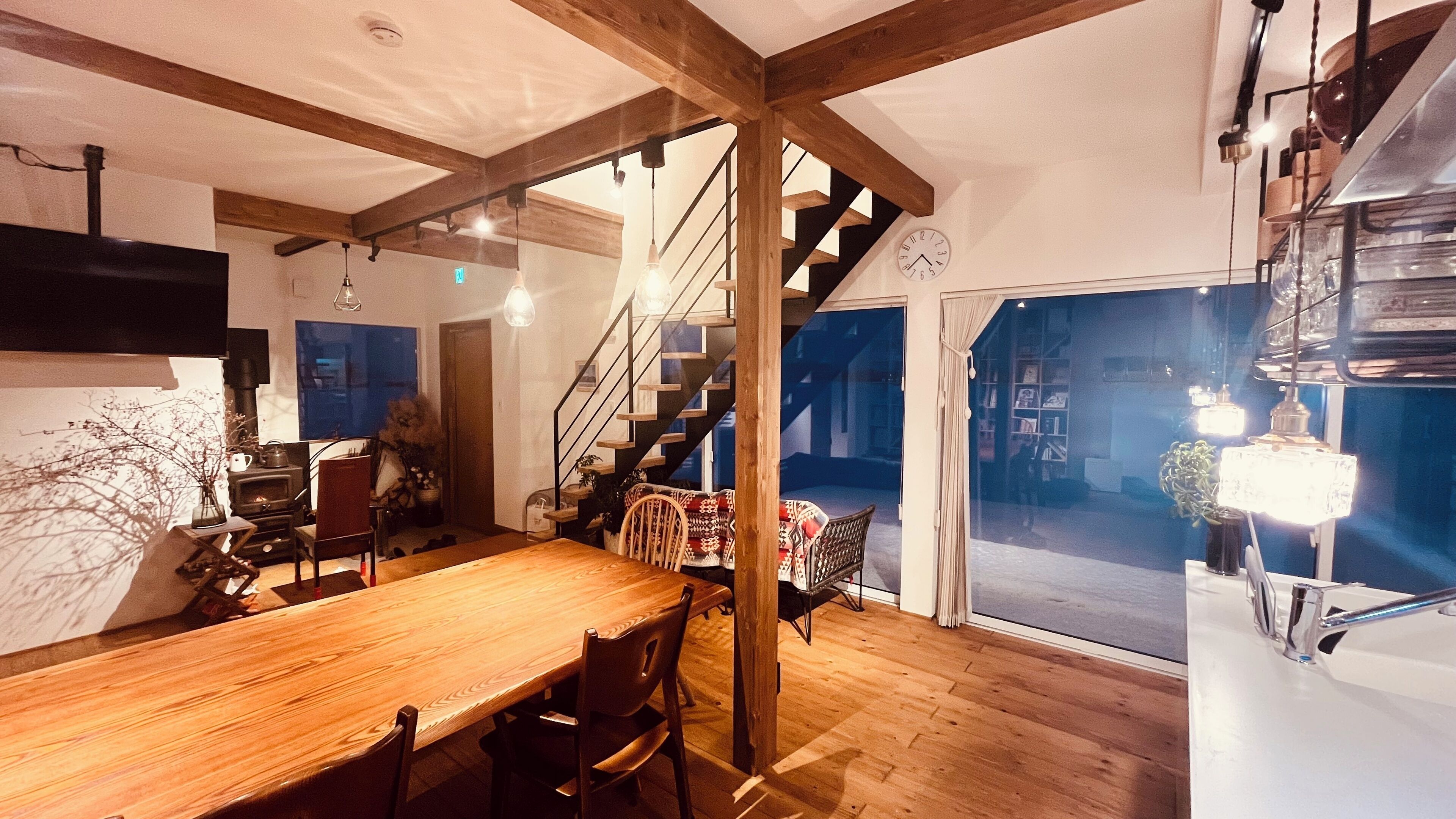 A cozy interior with a wooden dining table, chairs, a staircase, and a view through a glass door.
