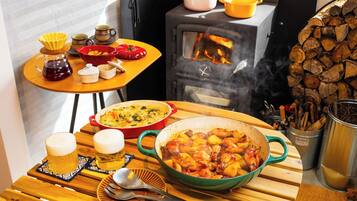 A rustic kitchen with a wood stove, cooking pots, and a dining table set for a meal.