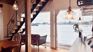 Un interior moderno con una escalera de madera, un comedor con mesa y sillas, un sofá con estampado, y vistas a un paisaje nevado a través de un ventanal grande.