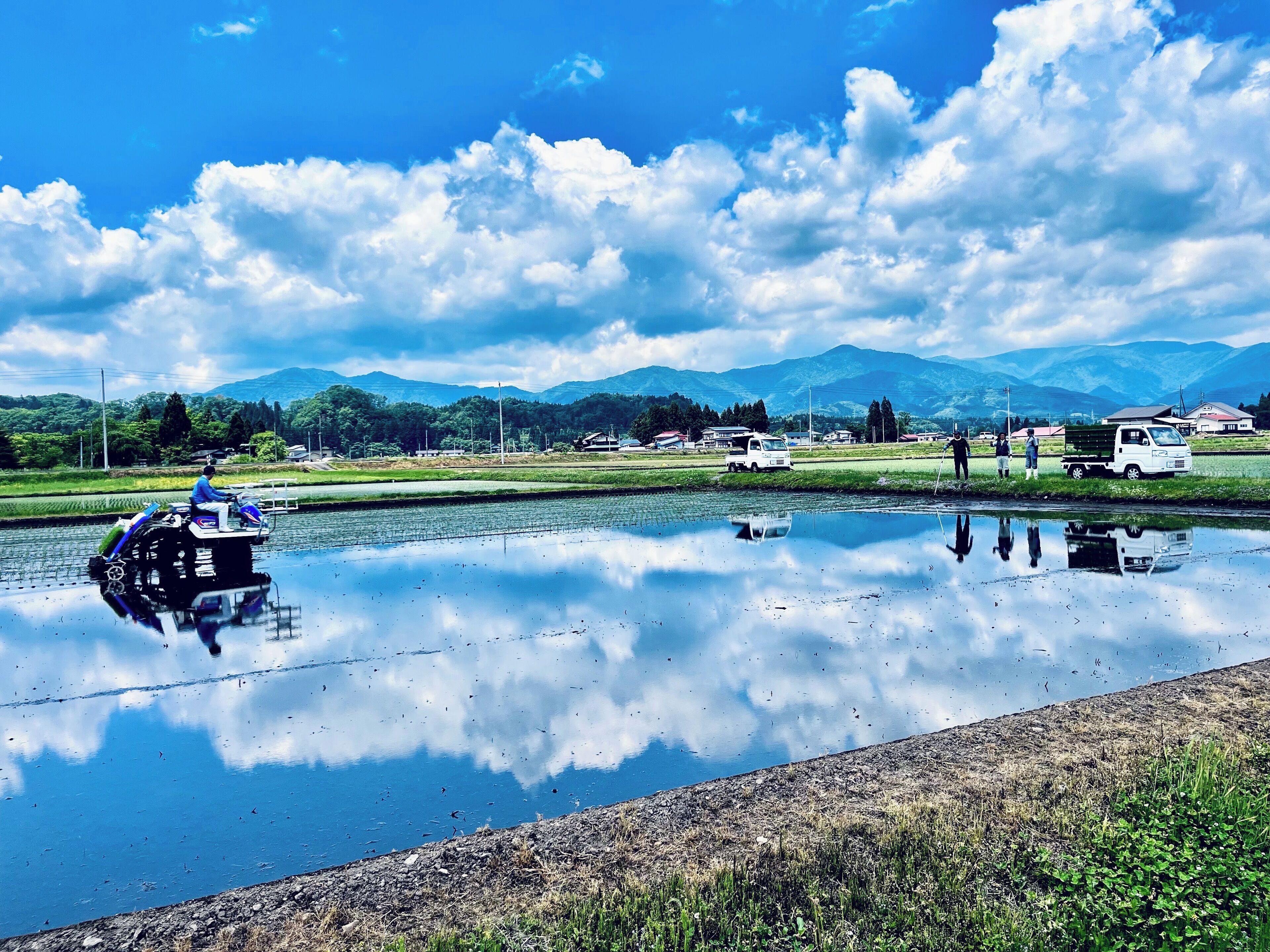 A calm water body with a motorboat, a truck, and a few people on the shore.