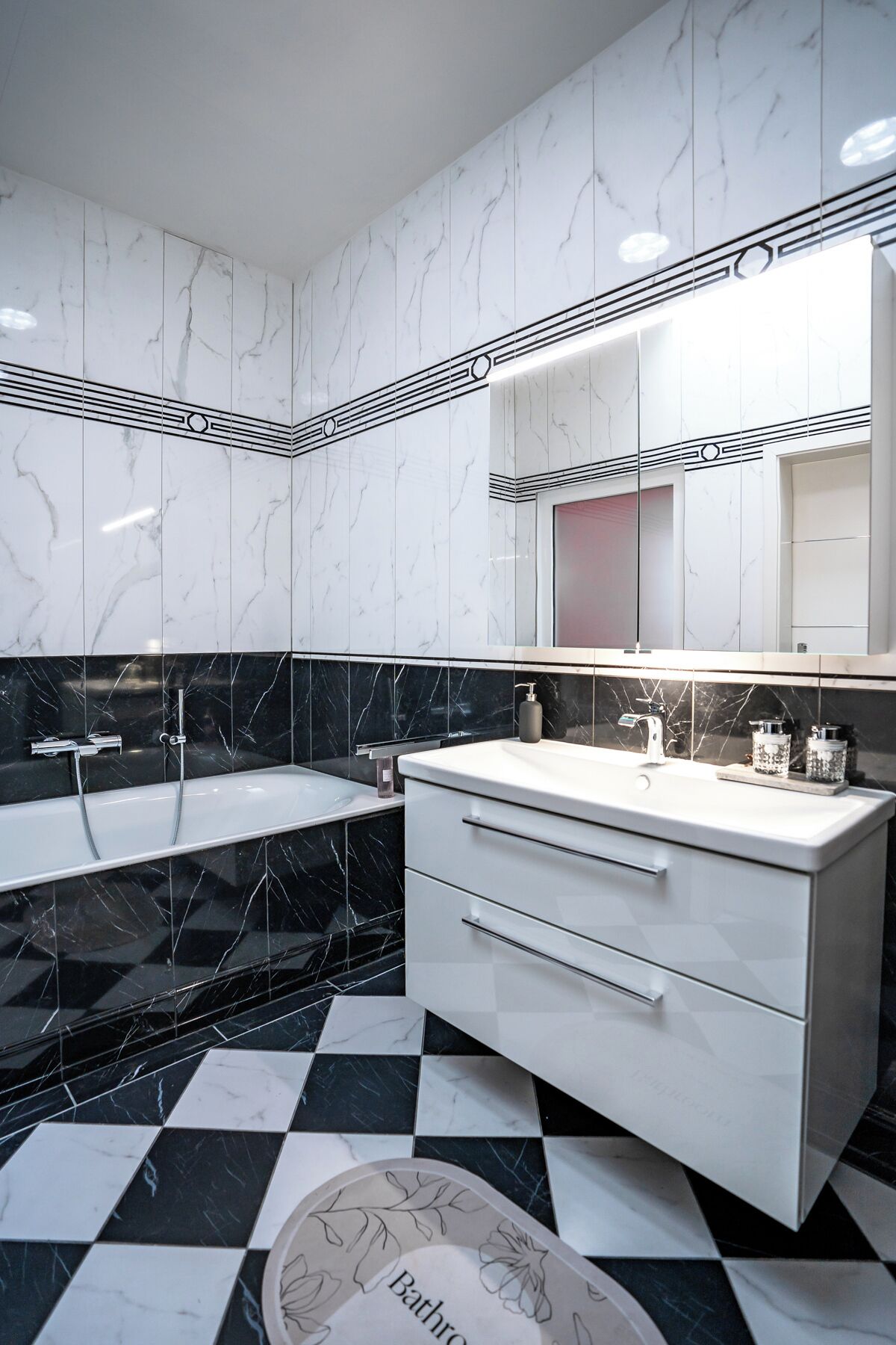 A modern bathroom with a black and white checkered floor, a white vanity with a mirror, and a bathtub with a black marble surround.