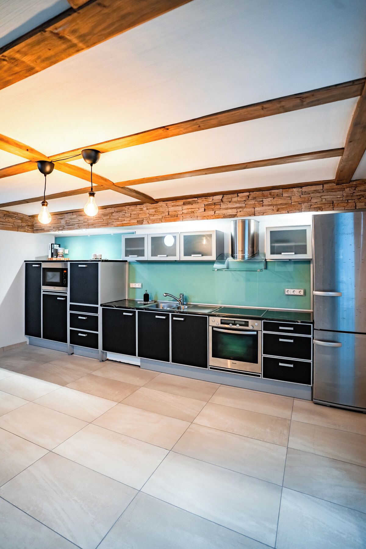 A modern kitchen with black cabinets, a stainless steel refrigerator, and a stone wall backsplash.