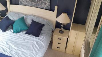 A bed with white bedding and three pillows, two bedside tables with lamps, and a small drawer unit.