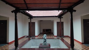 A covered corridor with a tiled ceiling, wooden pillars, and a statue in the center. - V NATURE RESORTS (Kanakapura)