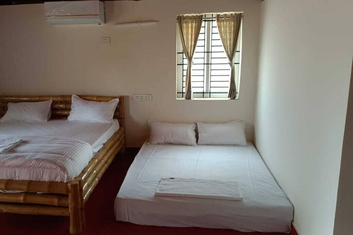 Two single beds with white linens, a window with curtains, and a wall-mounted fan.