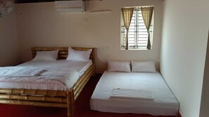 Dos camas individuales con sábanas blancas, una ventana con cortinas y un ventilador de pared.