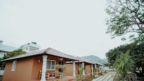 A two-story building with a tiled roof, a porch with seating, and a paved walkway. - V NATURE RESORTS (Kanakapura)