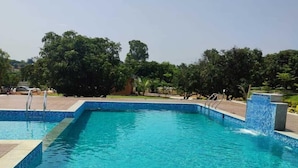 A rectangular swimming pool with clear blue water, surrounded by a tiled deck and a low brick wall. - V NATURE RESORTS (Kanakapura)