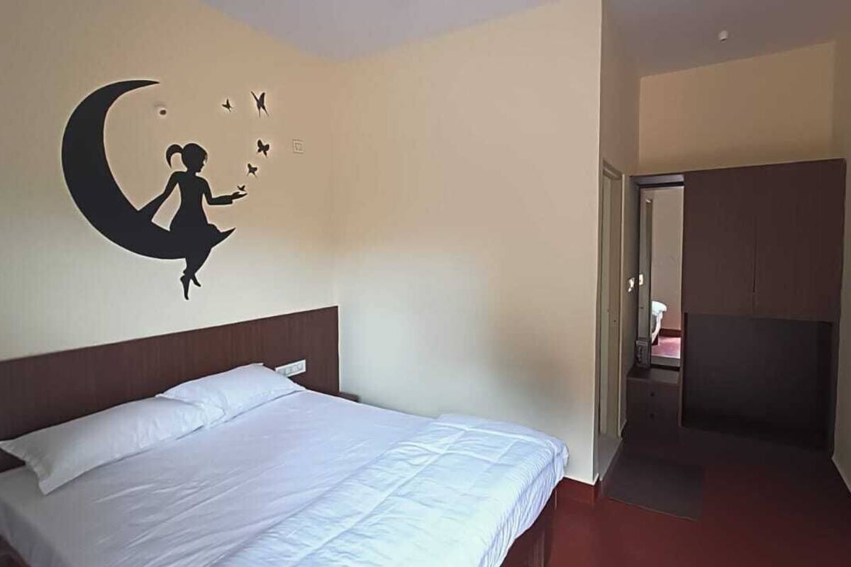 A hotel room with a bed, a wall mural of a girl on a crescent moon, and a door leading to a bathroom.