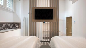 A hotel room with two beds, a TV mounted on a wall, a radiator, and a door to the right. - Contemporary Elegance: New 3-bedroom loft between Trastevere and the Vatican (Roma)