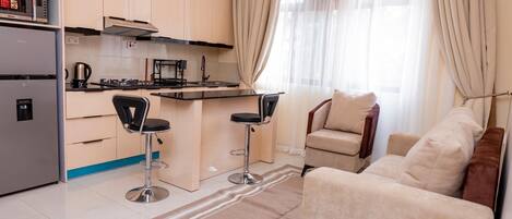 Un espacio habitable compacto con kitchenette, dos taburetes de bar, un sofá y una mesa de comedor.