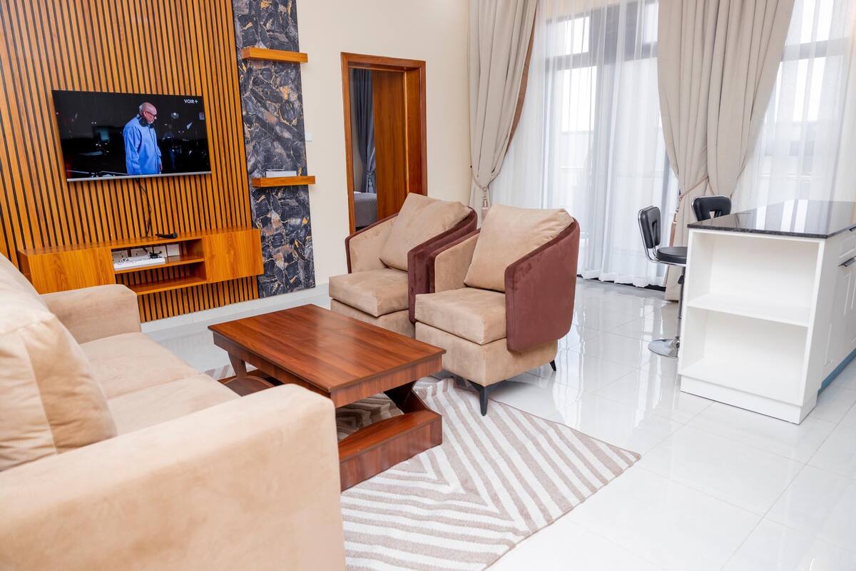 A modern living room with a TV, beige sofas, a wooden coffee table, and a white cabinet.