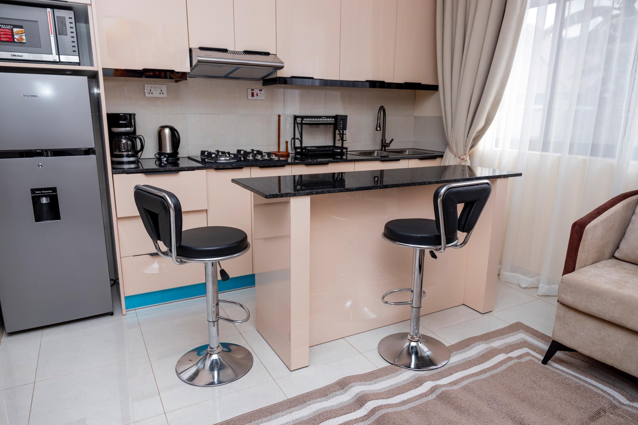 A compact kitchen with a refrigerator, microwave, coffee maker, and a small island with two bar stools.