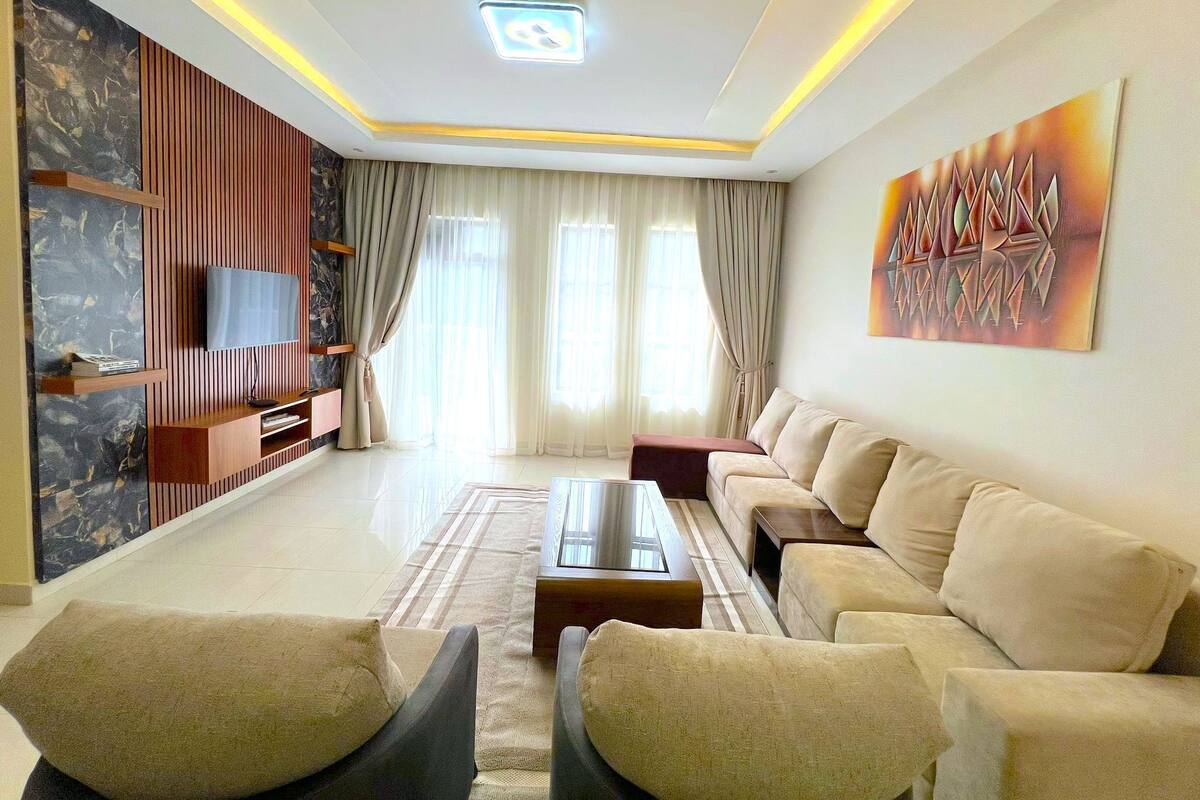 A modern living room with a sofa set, a coffee table, and a TV mounted on a wall with a decorative panel.