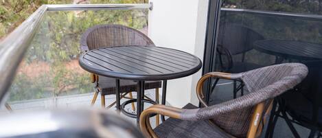 Un balcón con sillas de mimbre y una mesa redonda, con vistas a un jardín.