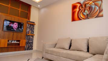 A modern living room with a beige sofa, a mounted TV, and a large abstract painting on the wall.