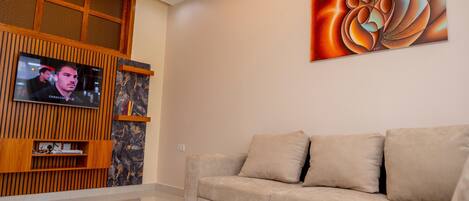 A modern living room with a beige sofa, a mounted TV, and a large abstract painting on the wall.
