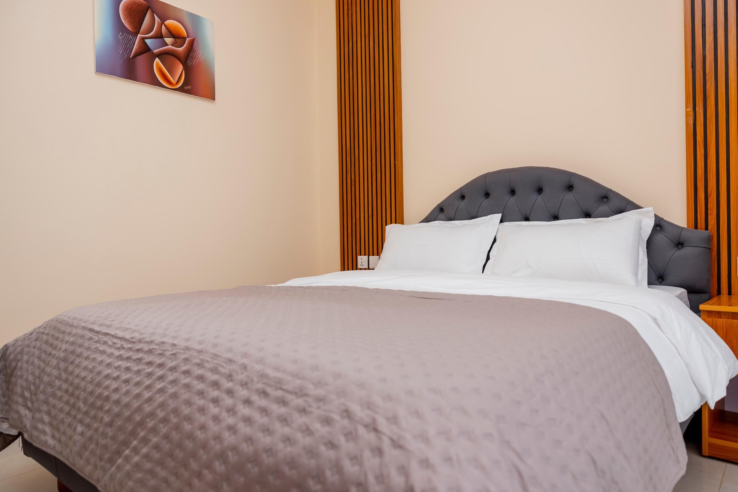 A neatly made bed with a grey headboard, a white pillow, and a grey blanket.