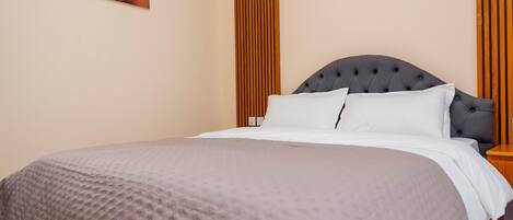 Una cama bien hecha con cabecera gris, almohada blanca y manta gris.