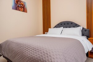Una cama bien hecha con cabecera gris, almohada blanca y manta gris.