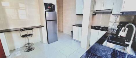 A modern kitchen with white cabinets, a stainless steel refrigerator, a black countertop, and a sink.