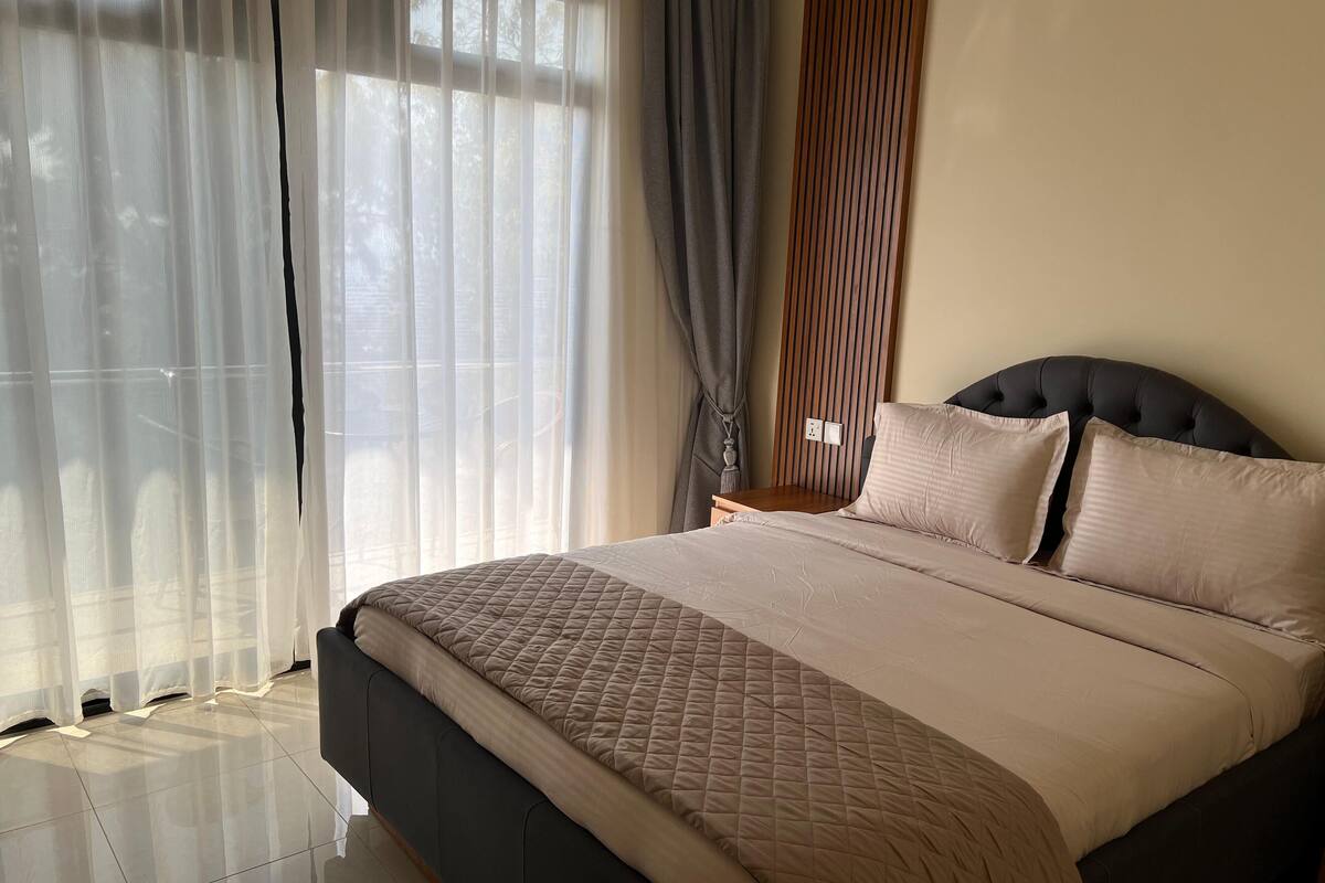 A neatly made bed with a quilted cover, a wooden headboard, and a nightstand with a lamp.