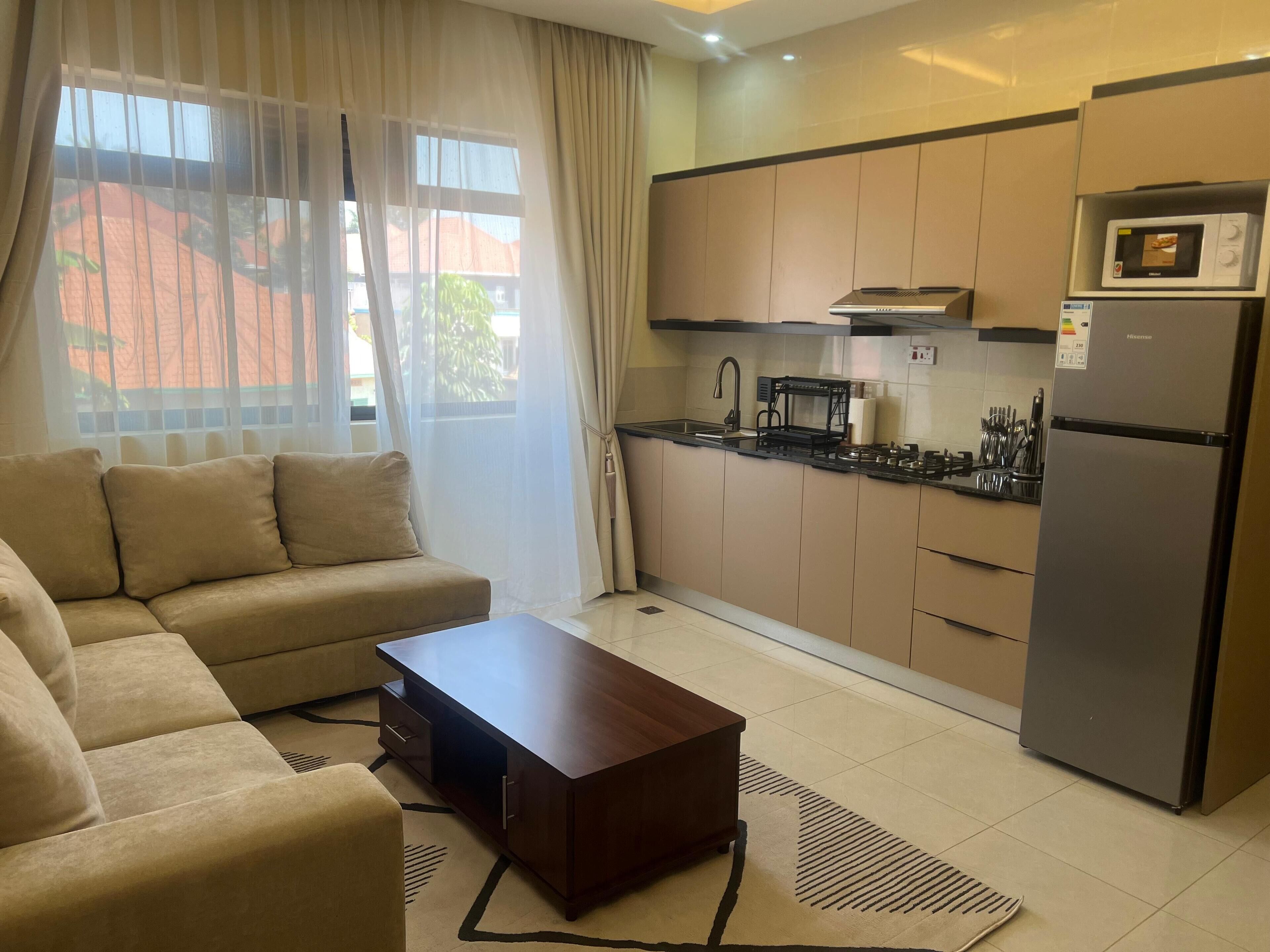 A modern kitchen with a built-in stove, microwave, and refrigerator. There is a sofa and a coffee table in the living area.
