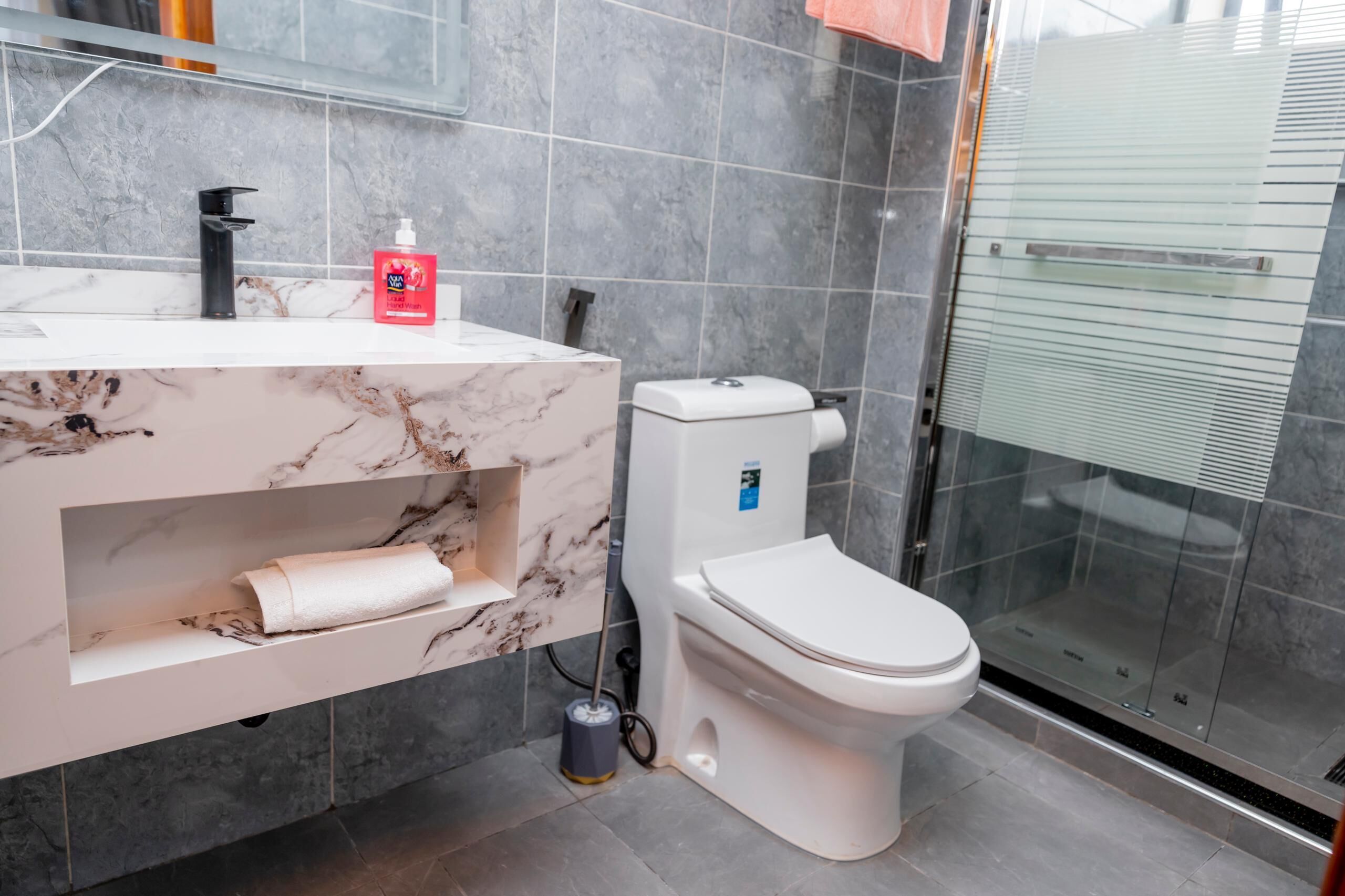 Une salle de bain moderne avec un meuble-lavabo en marbre, des toilettes et une cabine de douche en verre.