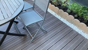 Una terraza de madera con una mesa redonda y una silla plegable.