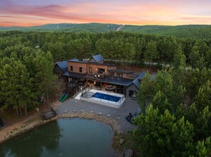 Una moderna casa a due piani con un'ampia terrazza, una piscina e vista su una zona boschiva.