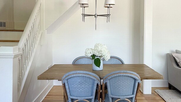 A dining area with a wooden table, four wicker chairs, a vase with flowers, and a modern chandelier. - Remodeled Downtown Cottage, close to St Clair River, McMorran, Convention Center (Port Huron)