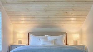 A bedroom with a wooden ceiling, a bed with white bedding, two bedside lamps, and a nightstand. - Remodeled Downtown Cottage, close to St Clair River, McMorran, Convention Center (Port Huron)