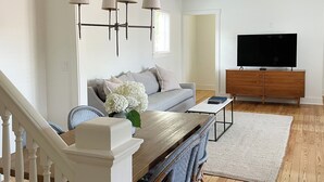 A modern living room with a dining area, wooden flooring, a white staircase, and a flat-screen TV. - Remodeled Downtown Cottage, close to St Clair River, McMorran, Convention Center (Port Huron)