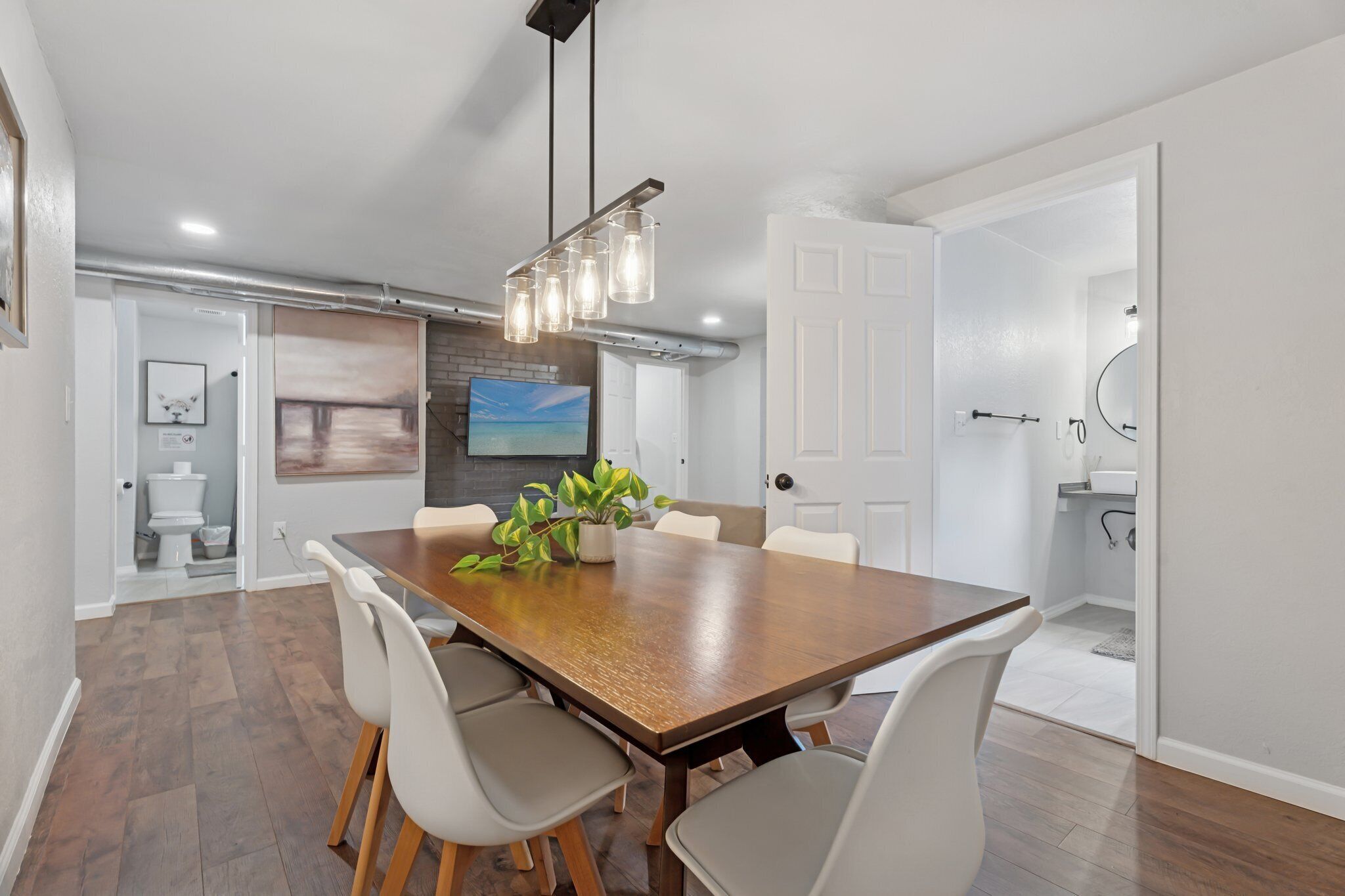 Stylish dining room with seating for six, modern pendant lighting, and abstract art—perfect for meals or remote work.