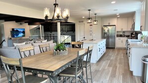 Una cocina moderna con armarios blancos, una isla central y un comedor con mesa de madera y sillas de metal.