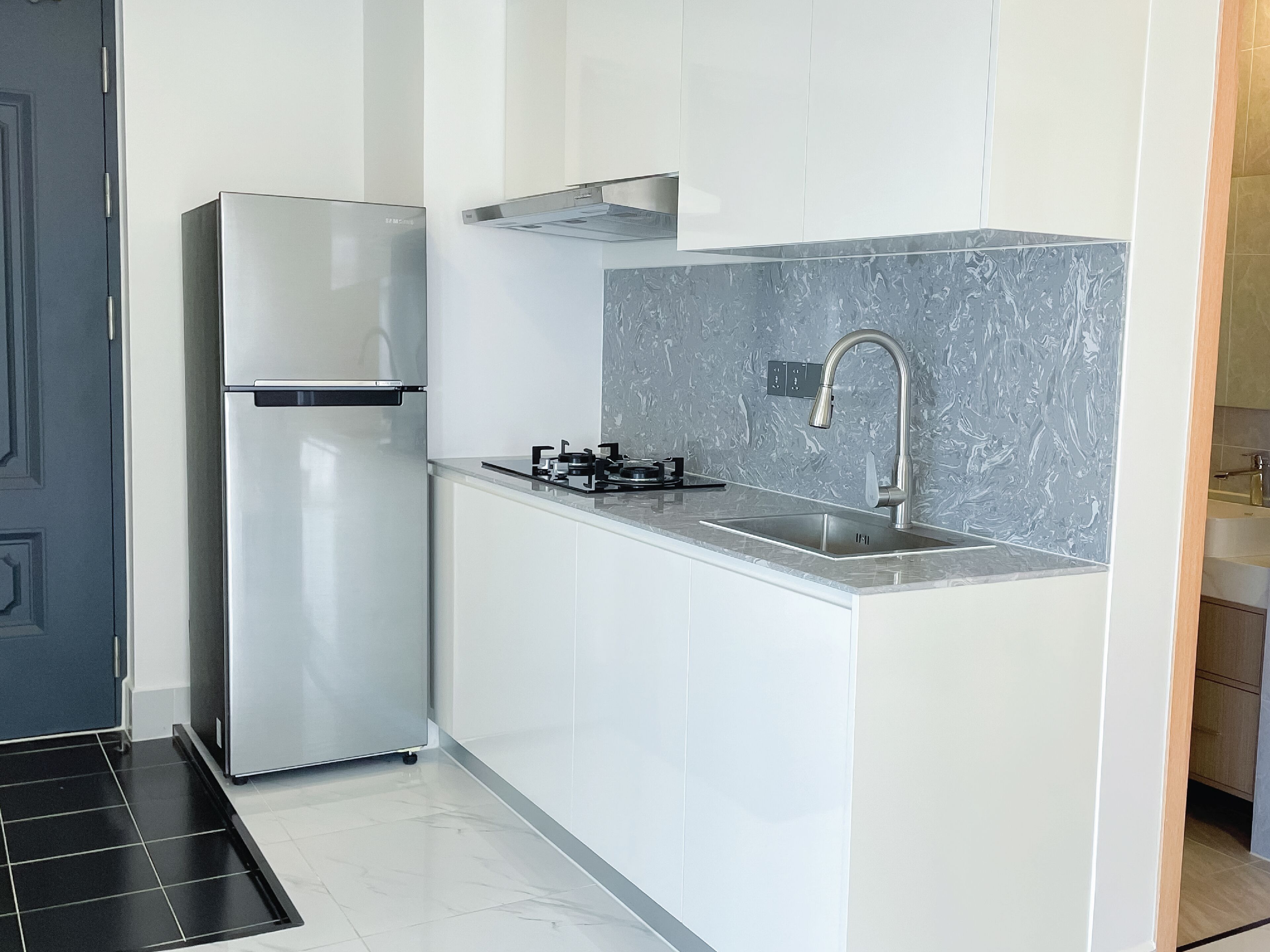 A compact kitchen with a stainless steel refrigerator, a gas stove, and a sink with a modern faucet.