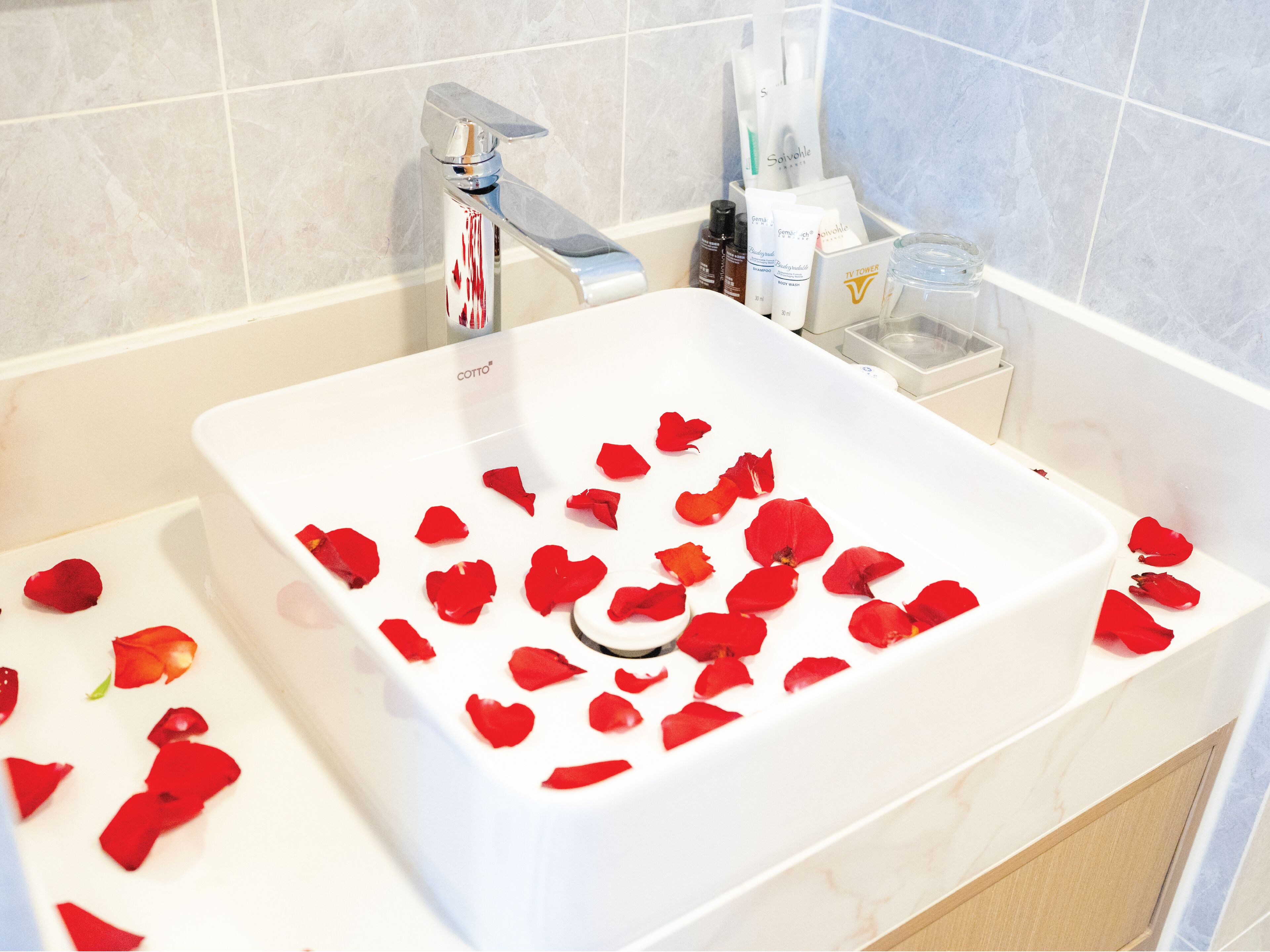A bathroom with a white sink, a silver faucet, and toiletries in a white container.
