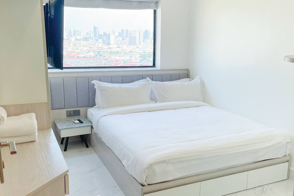 A modern hotel room with a bed, bedside table, and a window with a city view.